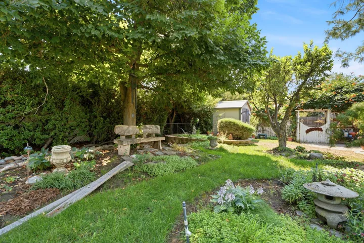 Expansive backyard featuring a mature tree, stone garden bench, manicured lawn, and a garden shed