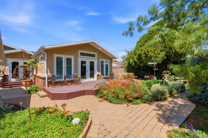 Exterior featuring stucco siding, multiple French doors, a raised deck, and brick paver pathways