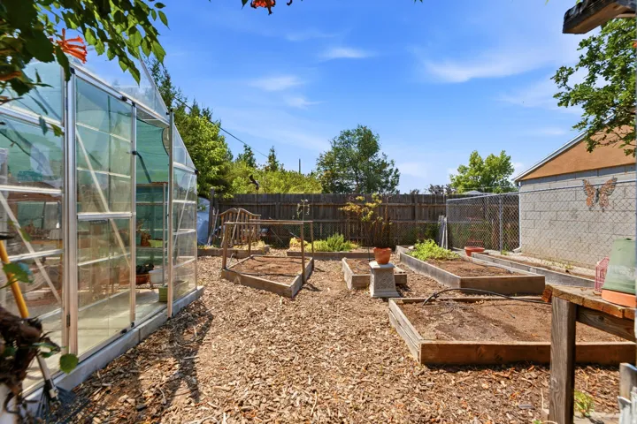 Spacious yard featuring a large greenhouse, multiple raised garden beds, wood chip ground cover, and block wall construction on an outbuilding