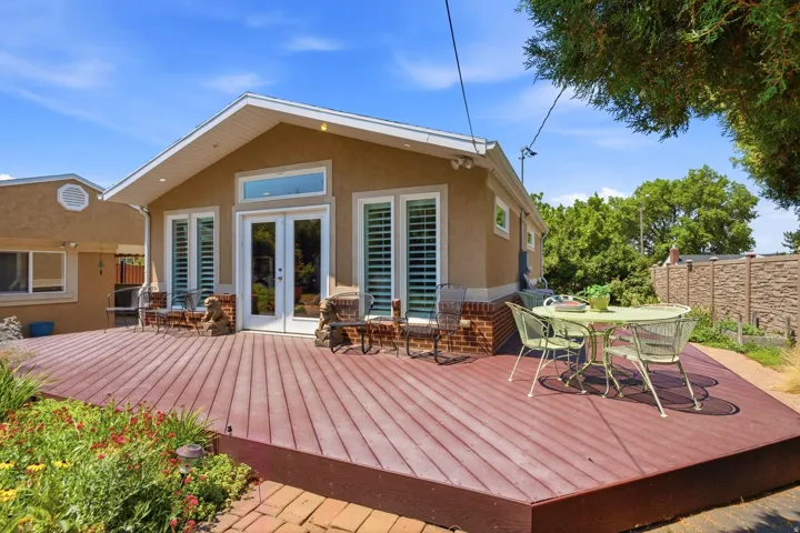 Expansive outdoor deck with a red-toned finish, featuring a stucco exterior with brick accents, white double doors, and transom windows