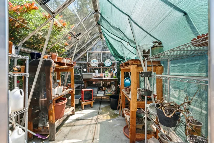 Greenhouse with clear panel roofing and a metal frame, featuring a partial shade covering