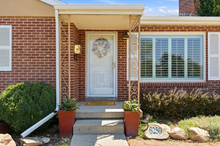 Brick exterior with white shutters, a covered entry with decorative metal railings, and a multi-pane window featuring interior plantation-style blinds