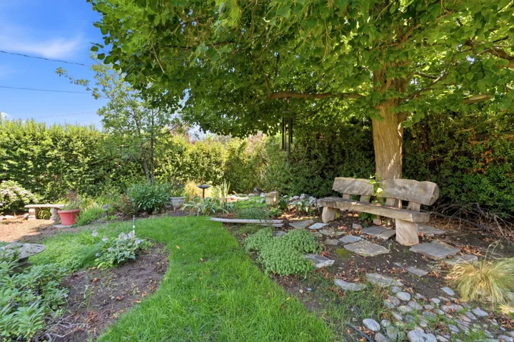 Landscaped garden path with a stone bench, mature trees, and privacy hedges