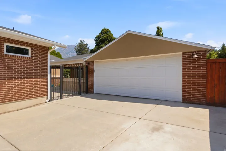 Concrete driveway with brick and stucco exterior, featuring a white paneled garage door and a wrought iron gate - 2 car garage