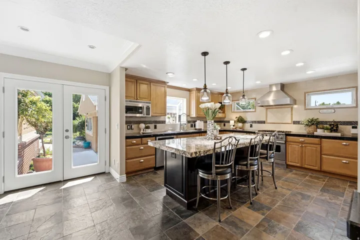 Kitchen featuring wood cabinetry, stainless steel appliances, a multi-tone stone flooring, a large island with seating, and recessed lighting
