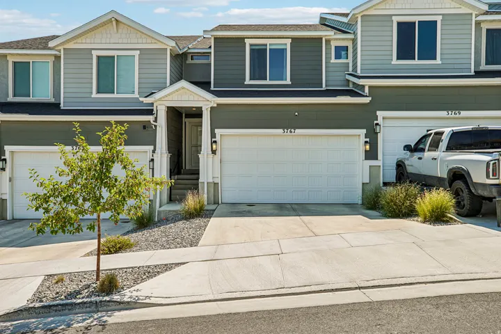Townhome exterior featuring multi-toned siding, white trim accents, prominent two-car garage, covered entry, and low-maintenance landscaping with decorative rock and mature plantings