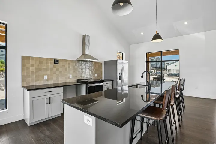 Kitchen featuring dark wood-finish flooring, white vaulted ceilings, and a large central island with a built-in sink and dark countertop