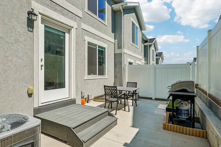 Modern rear patio featuring a composite deck with integrated steps, black metal outdoor seating, and direct access via French doors from the home's interior