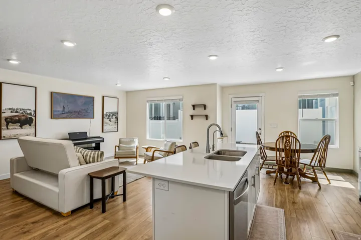 Open-concept living space featuring wood-finish flooring, recessed lighting, a kitchen island with a double basin sink and stainless steel dishwasher, and multiple windows providing natural illumination