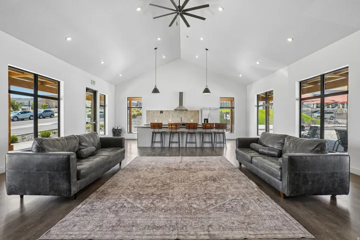 Open-concept living and dining area featuring dual charcoal gray upholstered sofas anchoring the space, wide-plank wood-finish flooring throughout, and a neutral area rug