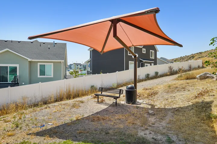 Outdoor shade structure with an orange fabric canopy, a dark-toned metal frame, a wooden bench, and a waste receptacle