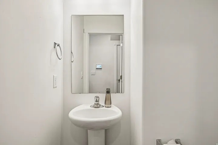 Clean and functional powder room featuring a round pedestal sink with chrome faucet and fixtures, framed mirror with integrated lighting, and bright white finishes throughout