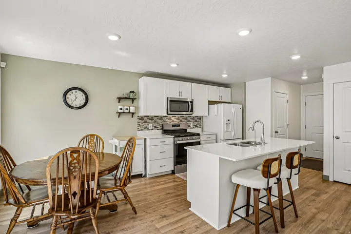 Open-concept kitchen and dining area featuring white cabinetry, stainless steel appliances, a tile backsplash, and a large center island with seating