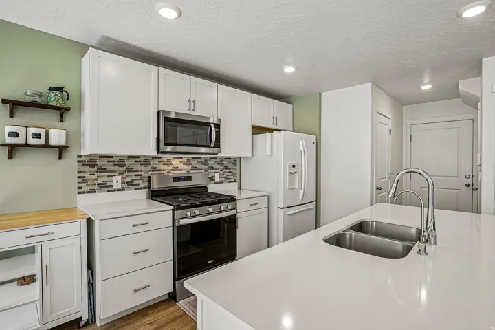 Modern kitchen featuring white cabinetry, stainless steel appliances including a gas range and over-the-range microwave, mosaic tile backsplash, and a large quartz island with waterfall edge