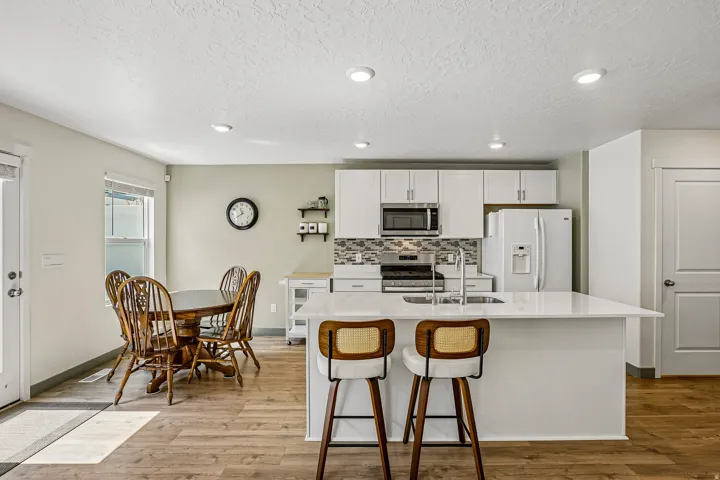 Open-concept kitchen featuring white cabinetry, stainless steel appliances, a white island with an integrated sink, patterned tile backsplash, and recessed lighting