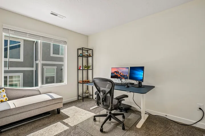 Modern home office featuring a spacious desk with dual monitor setup, ergonomic mesh office chair, and abundant natural light from large multi-pane windows
