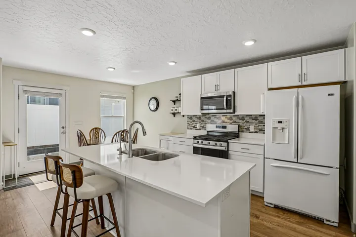 Modern kitchen featuring white cabinetry with stainless steel hardware, white quartz countertops, and a large waterfall-edge island with seating for three