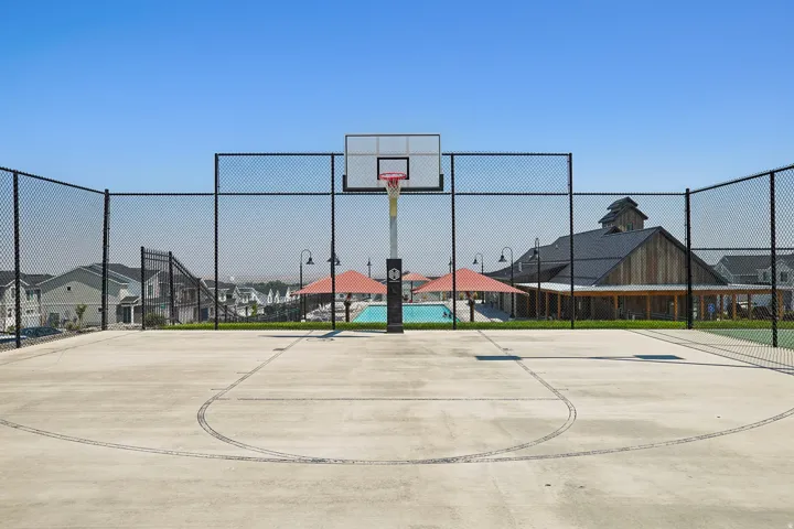 Paved sports court with a basketball hoop, surrounded by black chain-link fencing