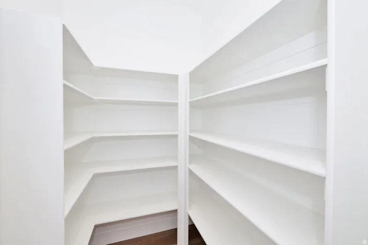 Walk-in pantry featuring white shelving, ample storage, and wood-finish flooring