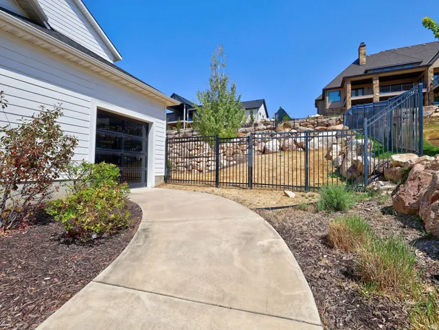 Curved concrete pathway leading to a garage with a full-view glass door, framed by landscaped bark mulch beds