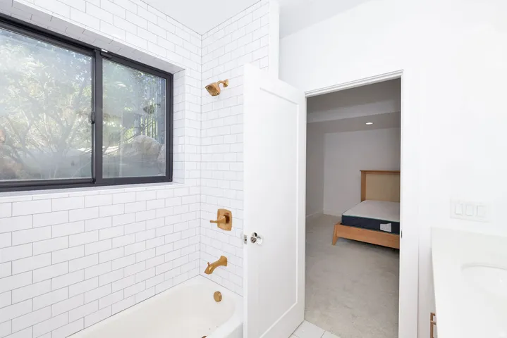 Bathroom featuring white subway tile surround, a built-in tub, and brass-finish fixtures