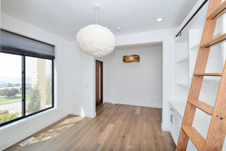 Room featuring wood-finish flooring, a contemporary white feather pendant light, and a large window with a roller shade