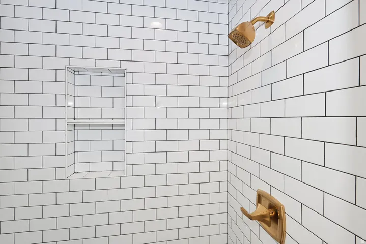 Shower with white subway tile walls, brushed gold fixtures, and an integrated tiled niche with shelving