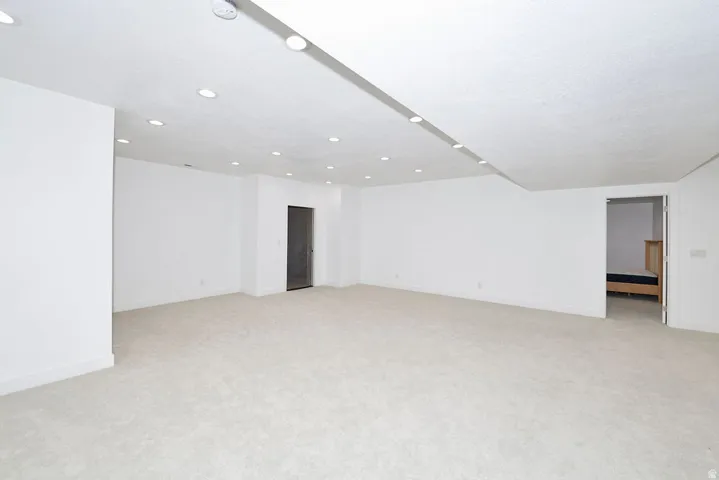 Spacious room featuring light-colored carpeting, white painted walls, recessed lighting, and white baseboards