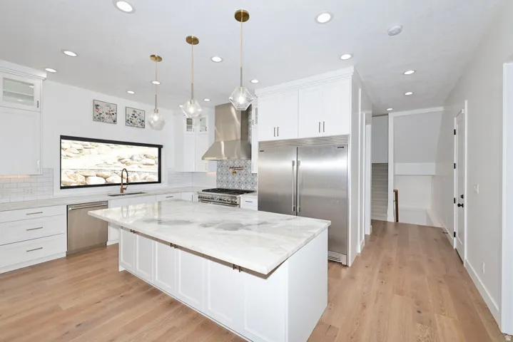 Contemporary kitchen featuring white cabinetry, a large center island with a stone countertop, stainless steel appliances, and wood-finish flooring
