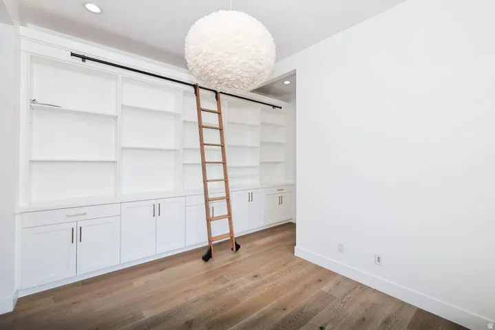 Custom built-in white cabinetry with open shelving and lower storage, featuring a rolling ladder on a black track system