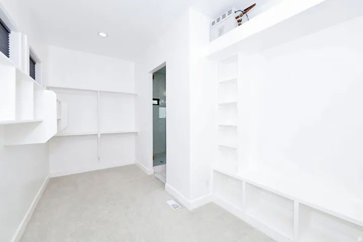 Bright room with light-colored carpeting, featuring built-in shelving, a recessed ceiling light, and a window with blinds