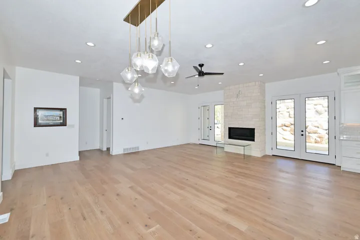Spacious open-concept room featuring light wood-finish flooring, a modern linear fireplace with stone surround, and multiple French doors providing abundant natural light