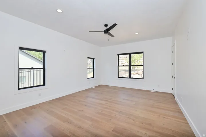 Spacious interior featuring light wood-finish flooring, white walls, multiple windows with black trim, recessed lighting, and a ceiling fan