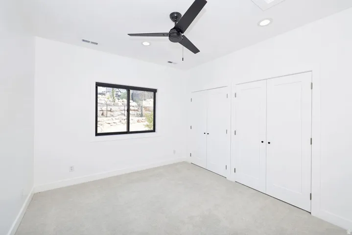 Bright interior space featuring light-toned carpeting, a black ceiling fan, recessed lighting, and a window with a black frame