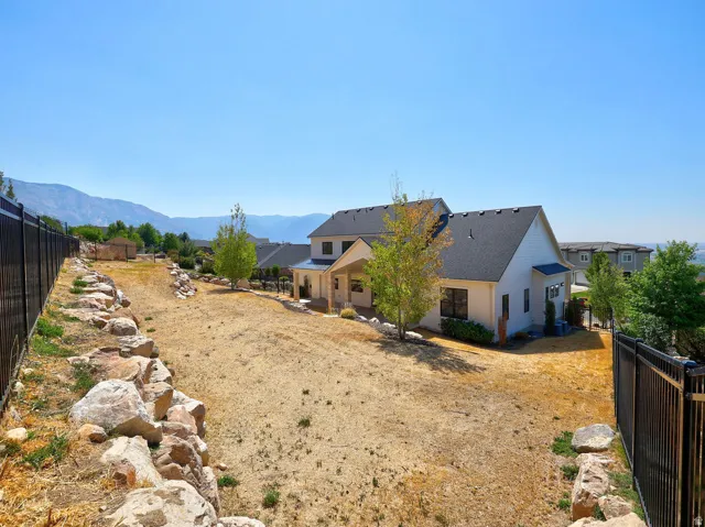 Expansive backyard featuring a black metal fence, rock retaining wall, and mountain backdrop