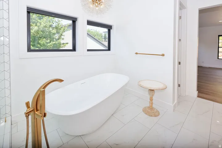 Freestanding soaking tub with a floor-mounted gold-tone faucet, complemented by white tile flooring