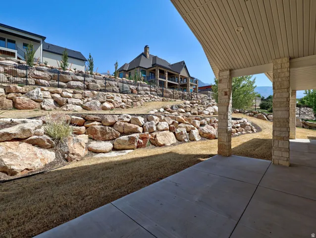 Covered patio with stone-wrapped columns, complemented by a terraced backyard featuring extensive rock landscaping and a perimeter fence