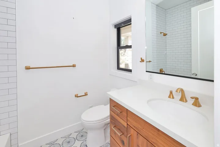 Modern vanity featuring wood-finish cabinetry, a white countertop with integrated sink, and gold-tone fixtures