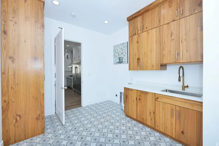 Utility room featuring wood-finish cabinetry, a sink with a bronze-finish faucet, and a light-toned countertop