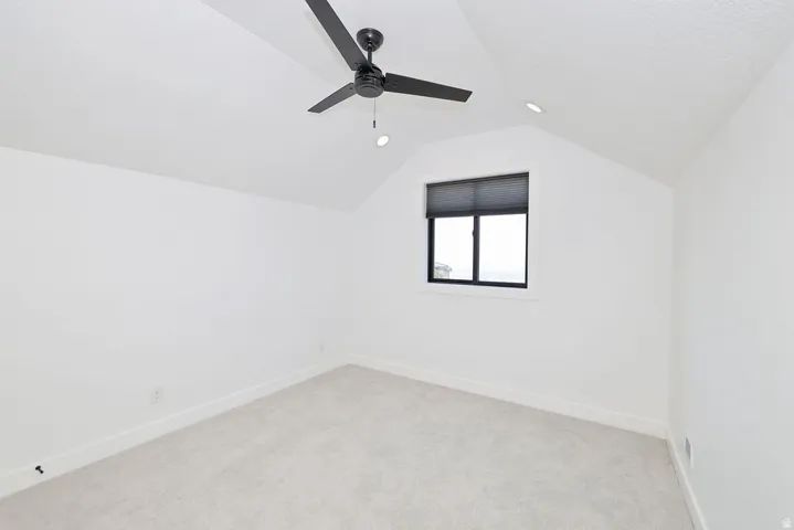 Light-filled room featuring a vaulted ceiling with a black ceiling fan, recessed lighting, a window with a black frame and dark shade, and light-colored carpet flooring