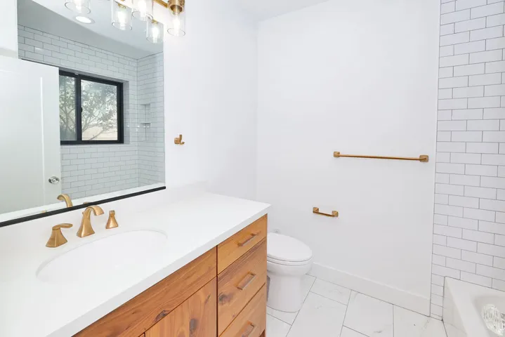 Bathroom vanity featuring a wood-finish cabinet, white countertop, and gold-toned fixtures