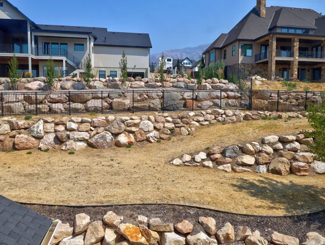 Terraced backyard featuring extensive rock retaining walls and a black metal fence