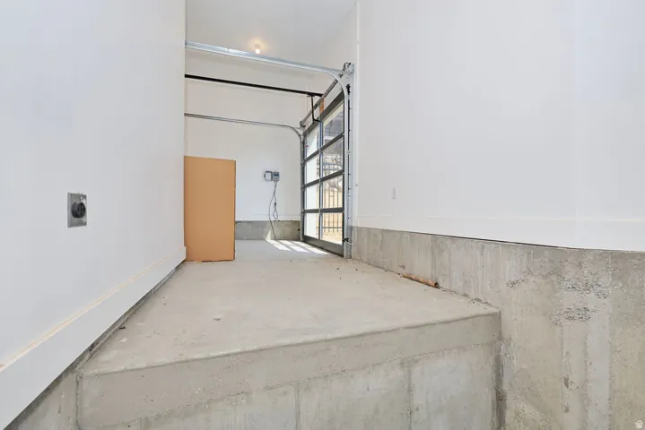 Concrete floor garage with a full-view glass garage door, white walls, and a visible electrical outlet