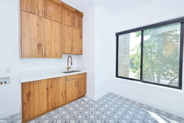 Dedicated wet bar featuring custom wood cabinetry with ample storage, a stainless steel sink with copper-finish faucet, white subway tile backsplash, and geometric patterned tile flooring