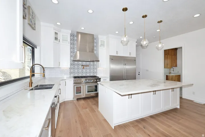 Gourmet kitchen featuring white cabinetry, light countertops, wood-finish flooring, a patterned tile backsplash, and stainless steel appliances