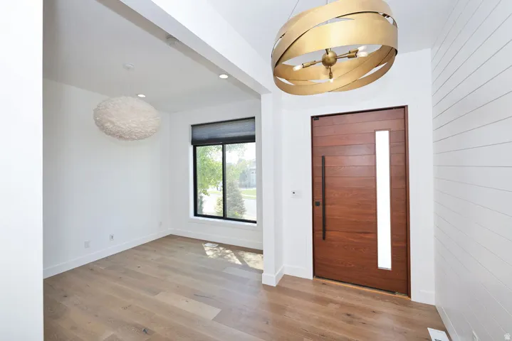 Entryway featuring wood-finish flooring, a contemporary wood door with vertical glass insert, white shiplap wall accent, and a modern gold-toned chandelier