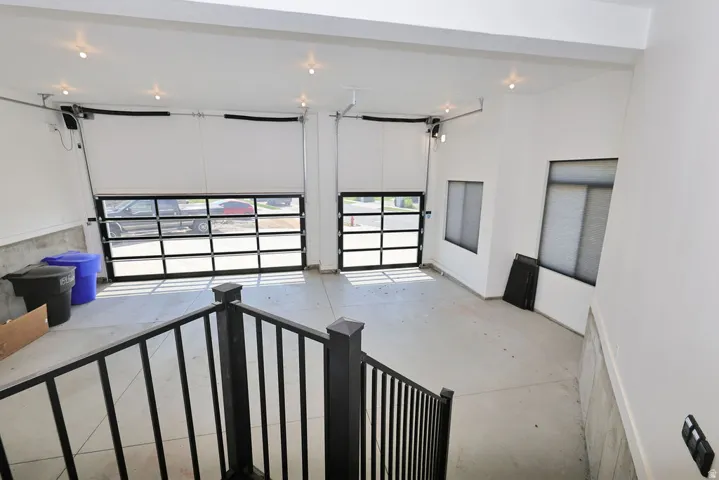 Two modern glass-paneled garage doors open to a spacious concrete-floored garage