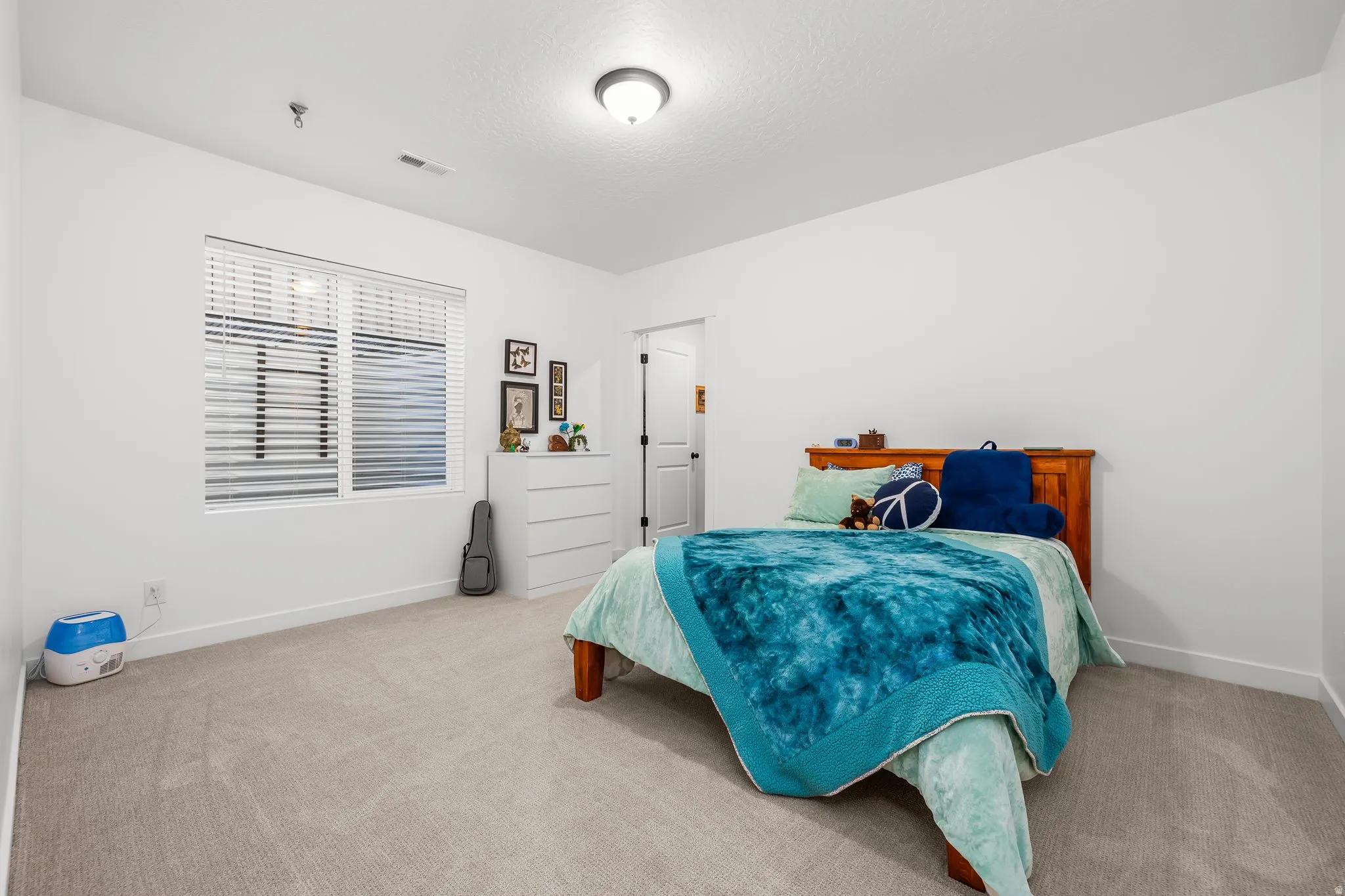 Bedroom featuring a rectangular window with horizontal blinds, neutral-toned carpet flooring, white painted walls, a flush-mount ceiling light fixture, and a white baseboard trim