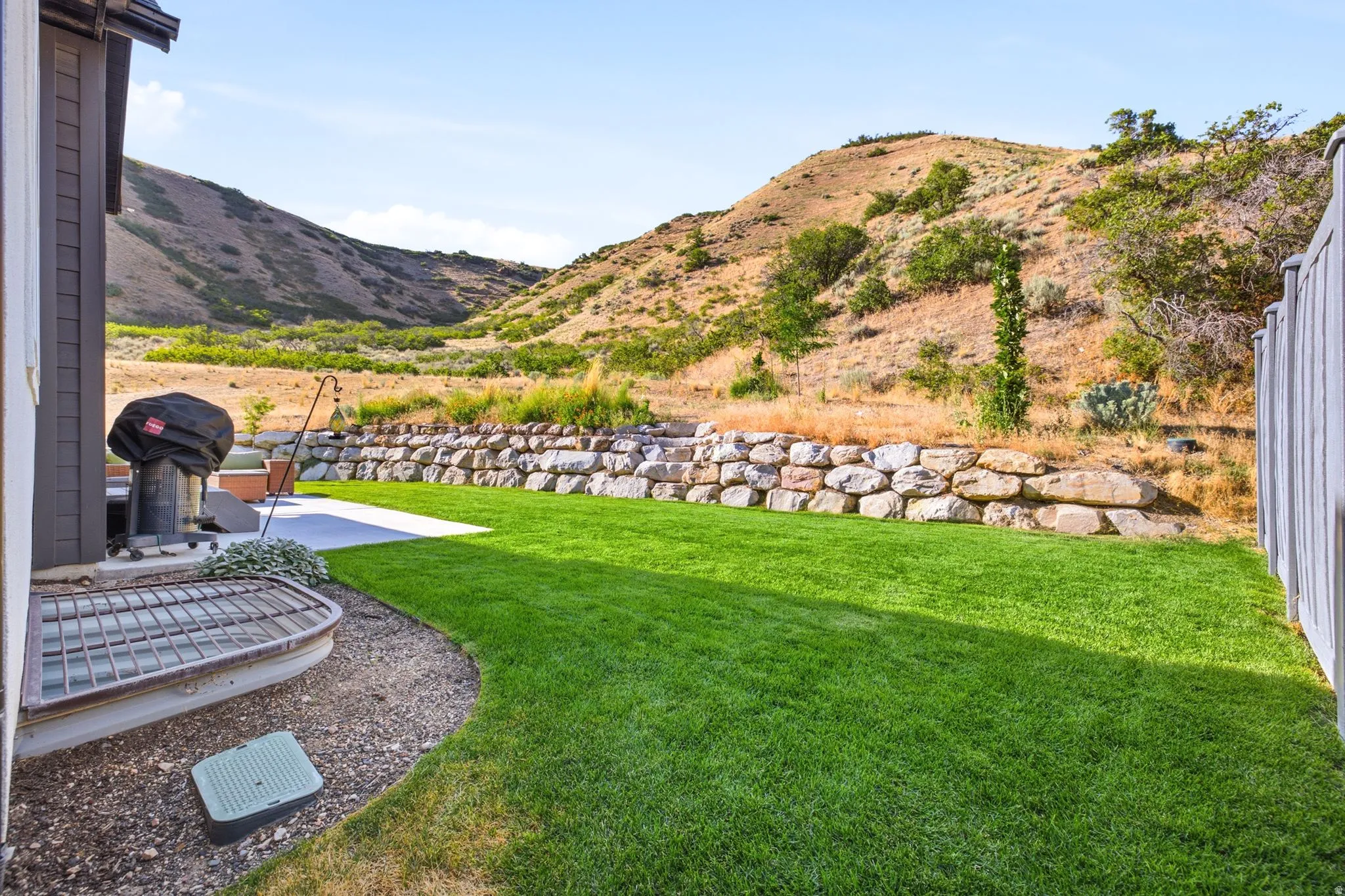 Expansive backyard featuring a lush lawn, concrete patio, and a stone retaining wall