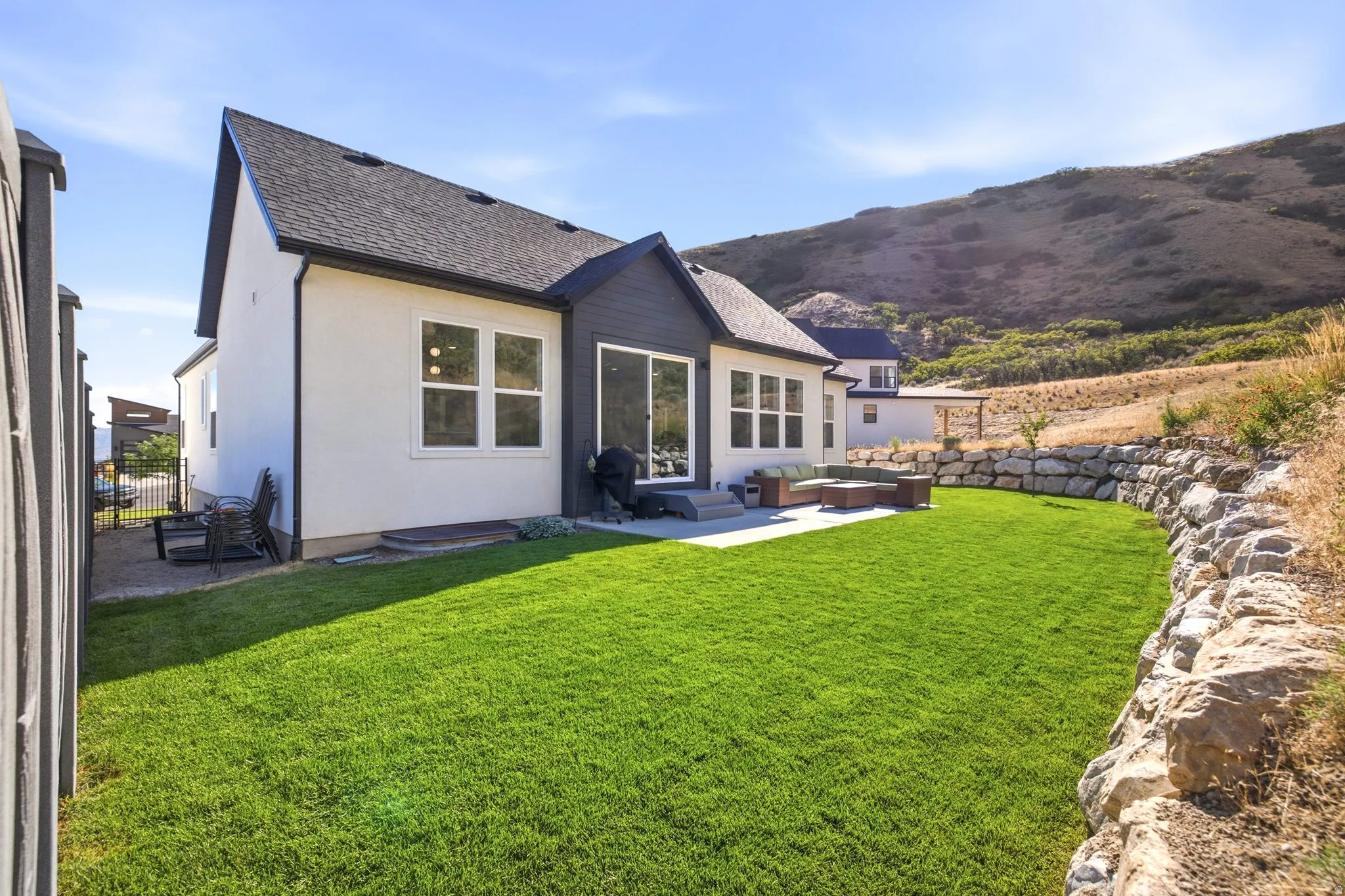 Expansive backyard featuring a manicured lawn, a large concrete patio, and a natural rock retaining wall